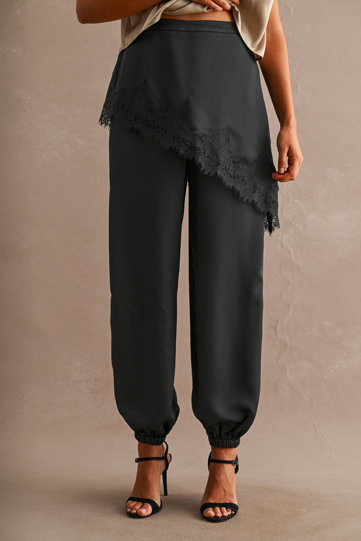 Front view of black satin joggers with asymmetric lace overlay panel