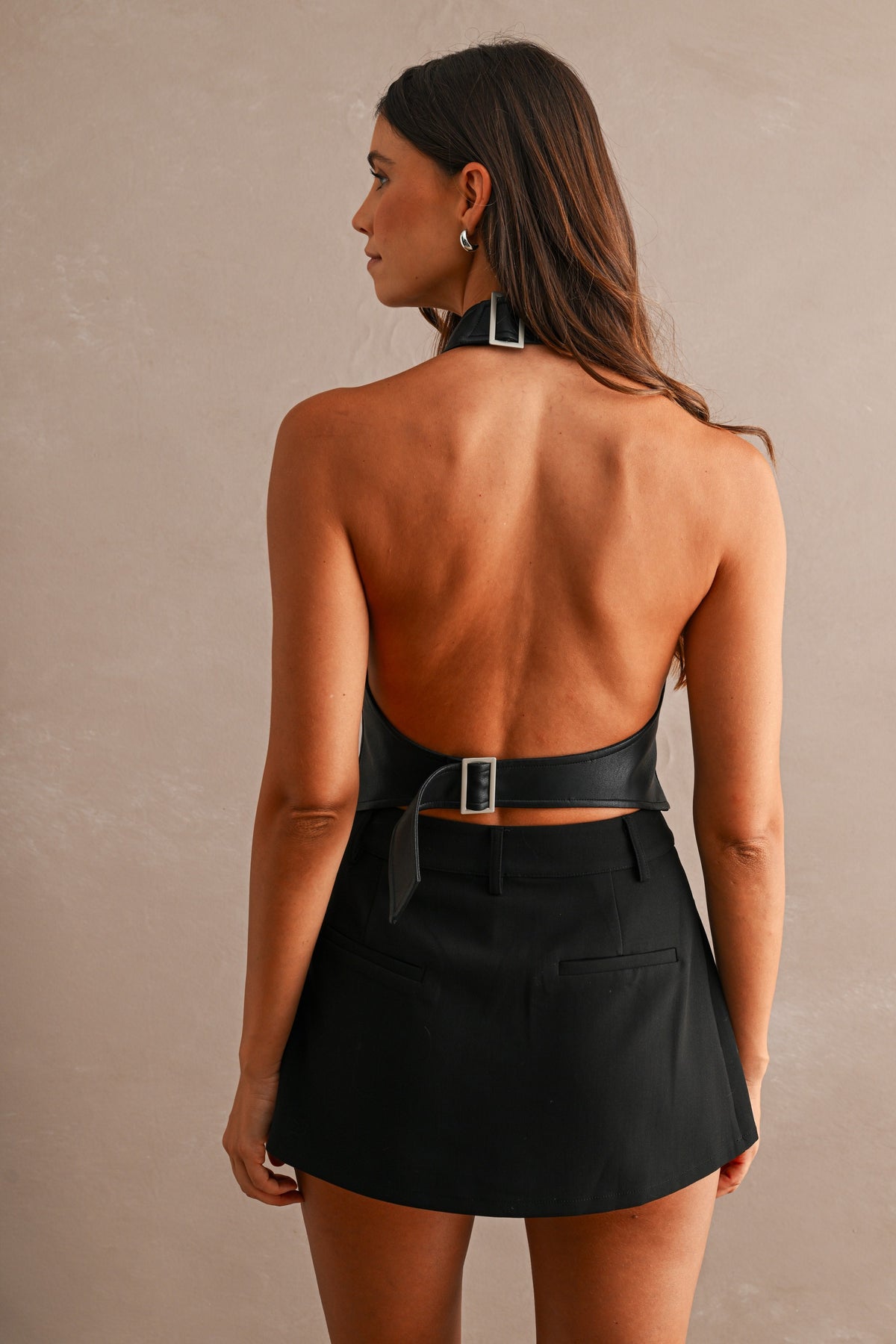 Open back of black faux leather halter top with buckled waist strap